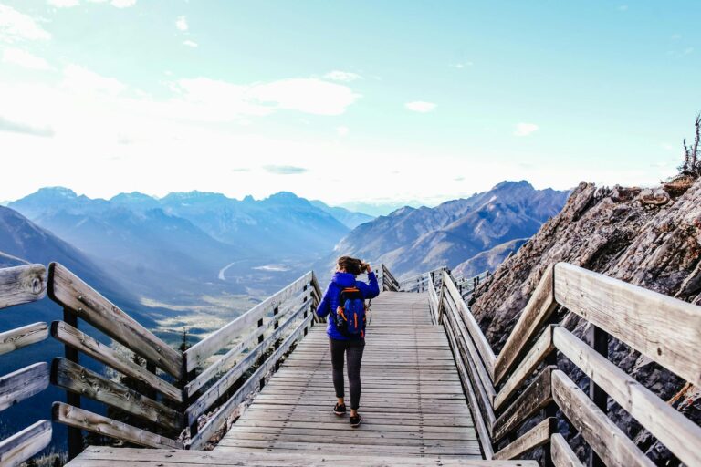 A woman hikes on a scenic mountain viewing deck surrounded by majestic ranges.